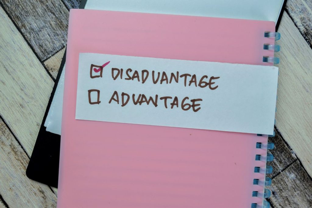 words disadvantage and advantage written on white piece of paper on a pink notebook