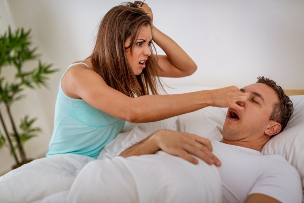 woman with irritated look on her face pinching the nose of the man beside her in bed