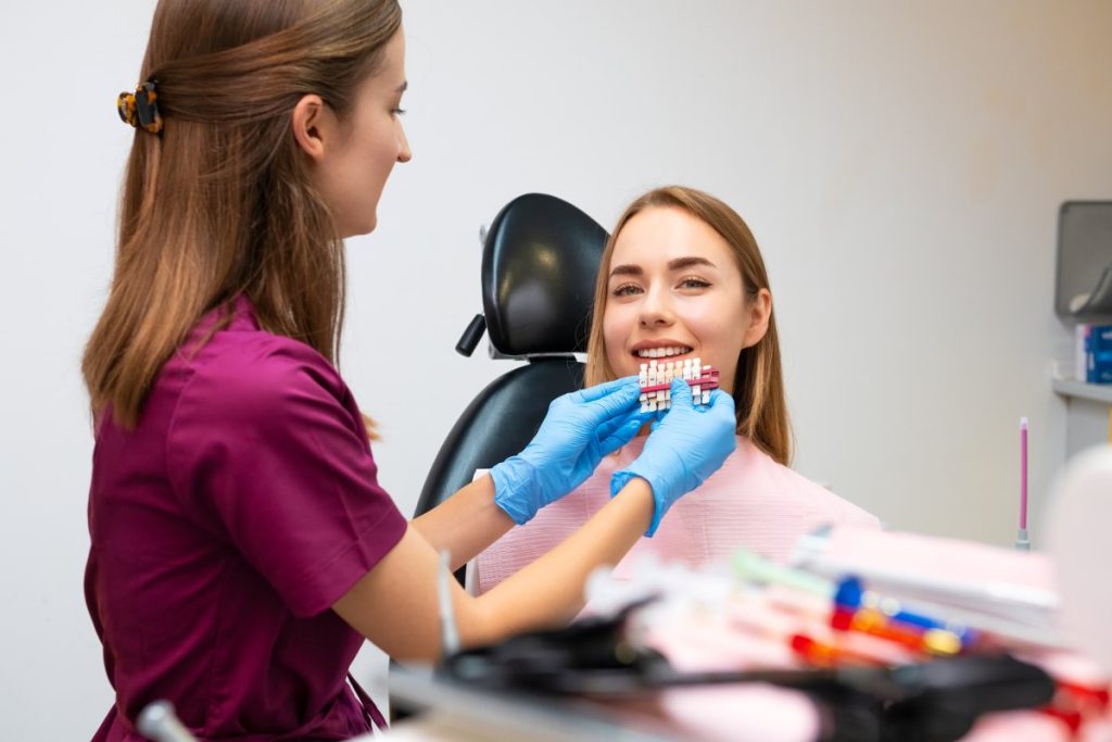 Dentist uses shades of tone for whitening of teeth and perfect woman smile for patient